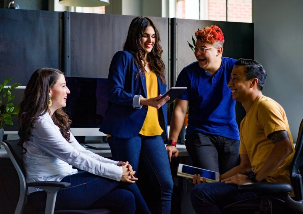 Group of four happy professionals in the workplace gathered together with two digital tablets.