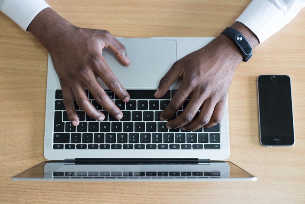 Top view of a man’s hands typing on a laptop keyboard.