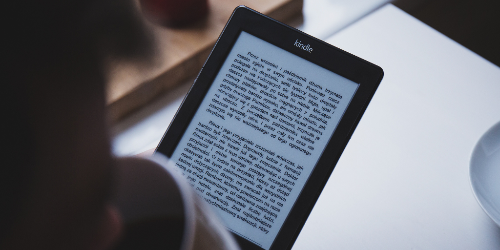 Person sips from coffee cup and reads text on an ereader device.