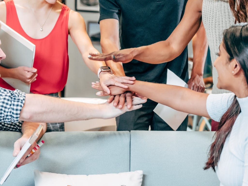 Team of professionals gather together to place hands in the center of the group.