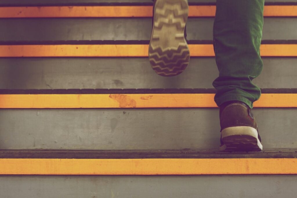 Person wearing brown suede shoes and jeans climbs stairs in a public place.