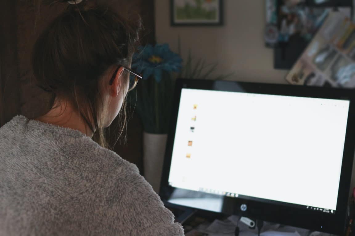 Woman with messy brown hair, glasses and a fuzzy gray shirt looks at her computer screen.