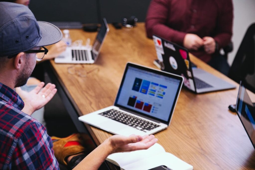 A group of 4 people sit at a table together in discussion with open laptops in front of each person.