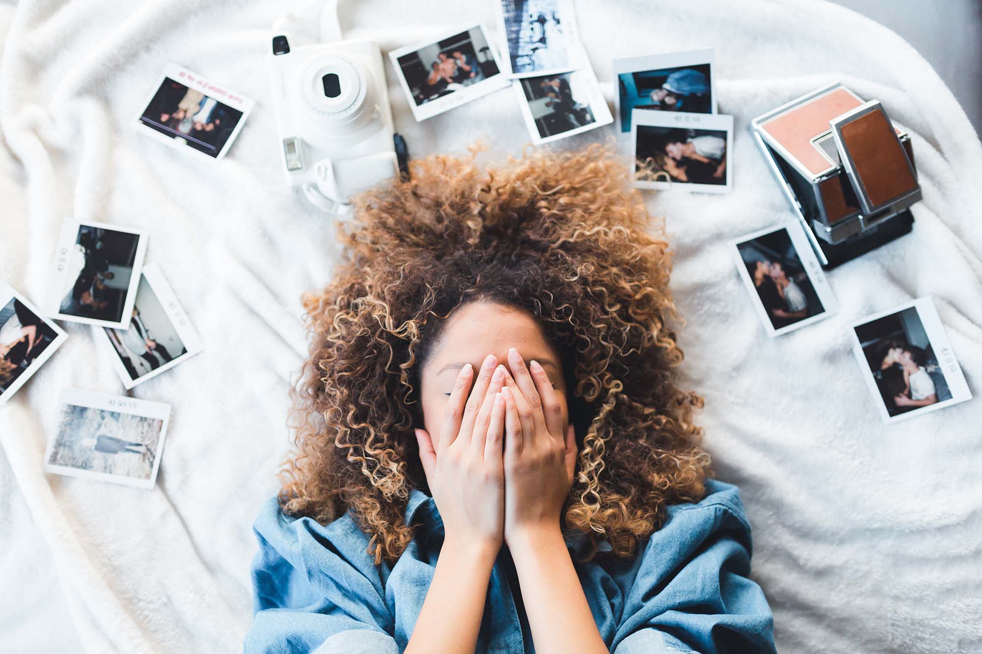 Social Media Graphics, Woman covering her face with her hair and many polaroid photos spread out on a crisp white bed