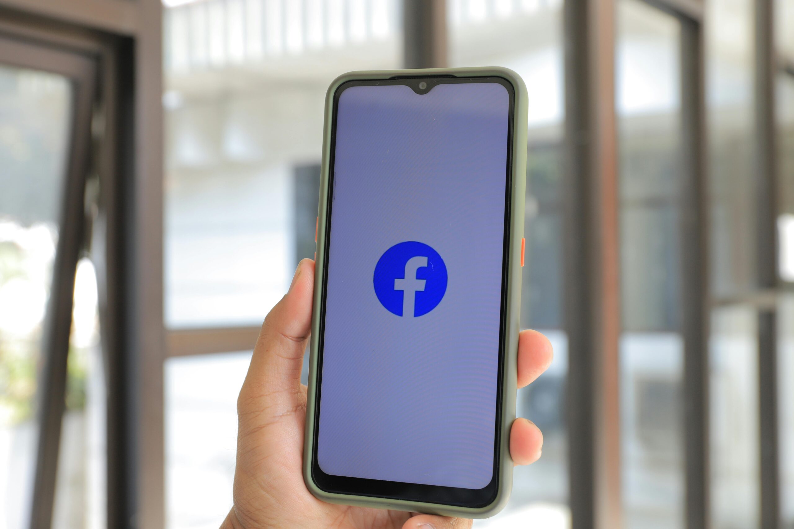 Facebook ad graphics, image of a hand holding a phone with the Facebook icon on the screen.