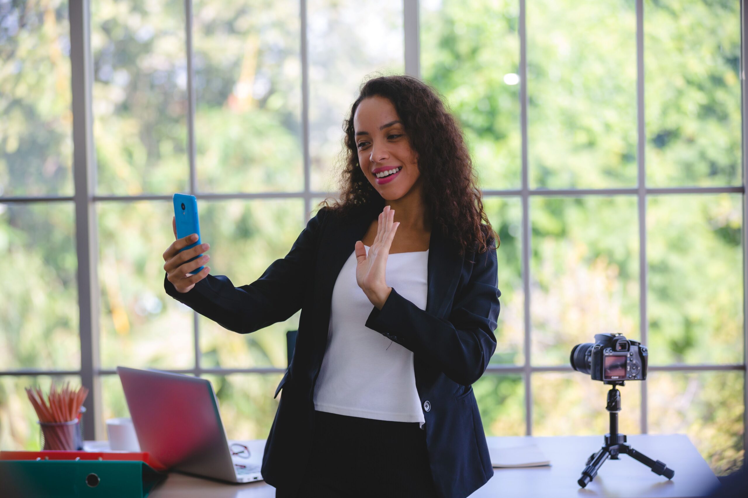 Alt text, Hashtags, image of a business woman using the phone to film herself in front of her desk that holds an open laptop and camera on a stand.