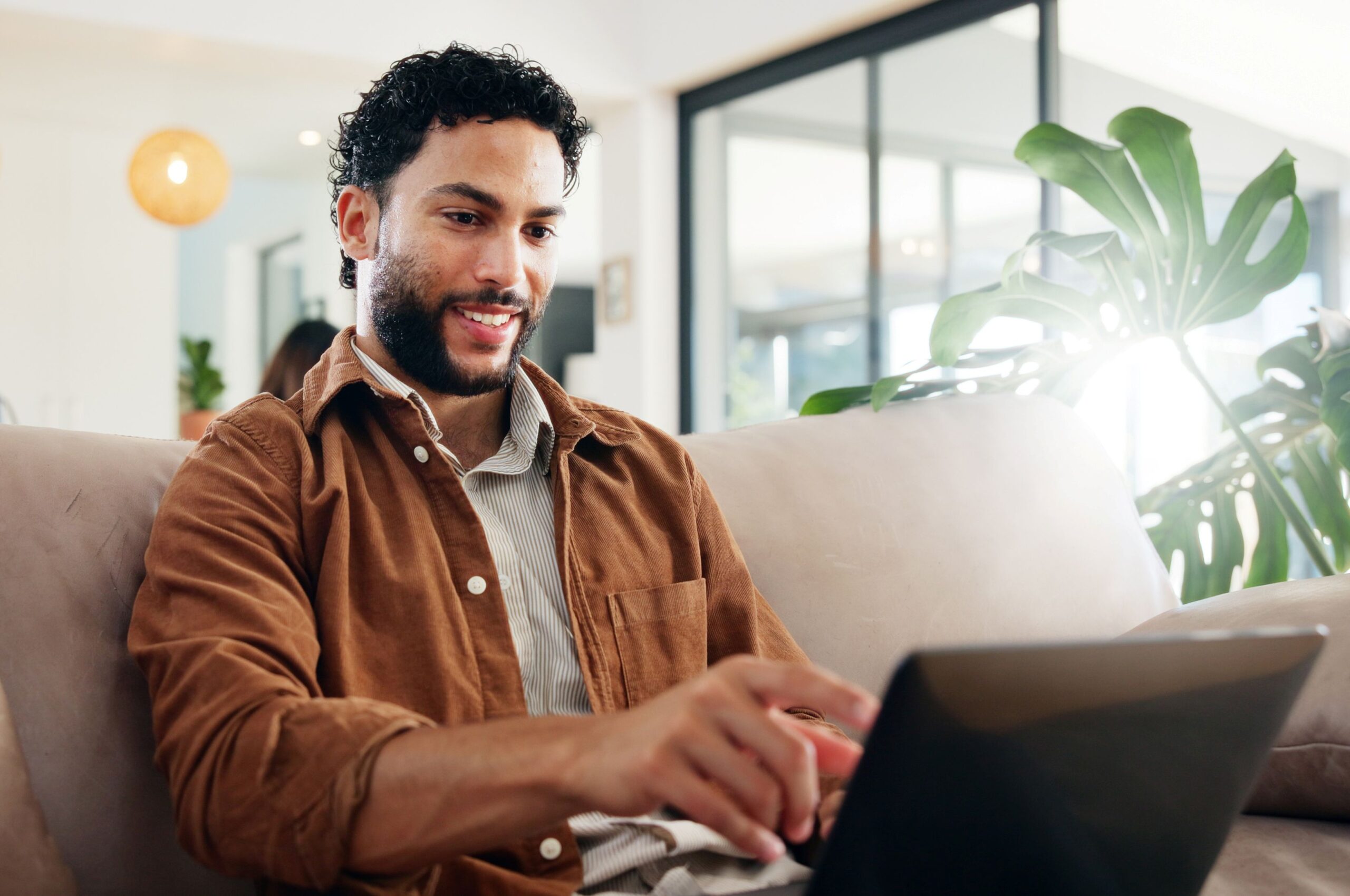 Alt text, Hashtags, image of a man wearing a camel color button-down shirt sitting on a couch using his laptop.