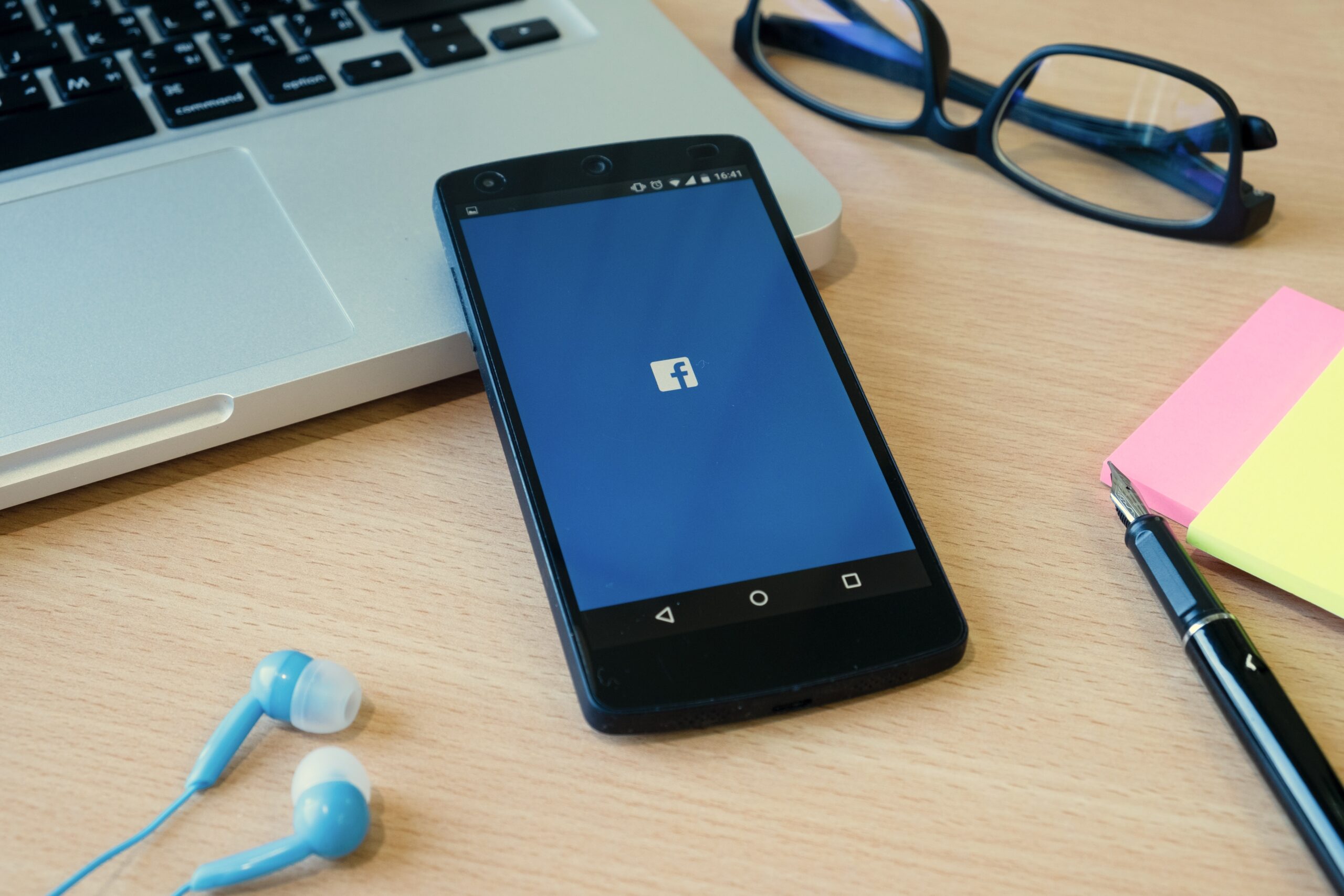 Important Meta Update, image of a smartphone with Facebook opened resting on a laptop with other office supplies surrounding it.