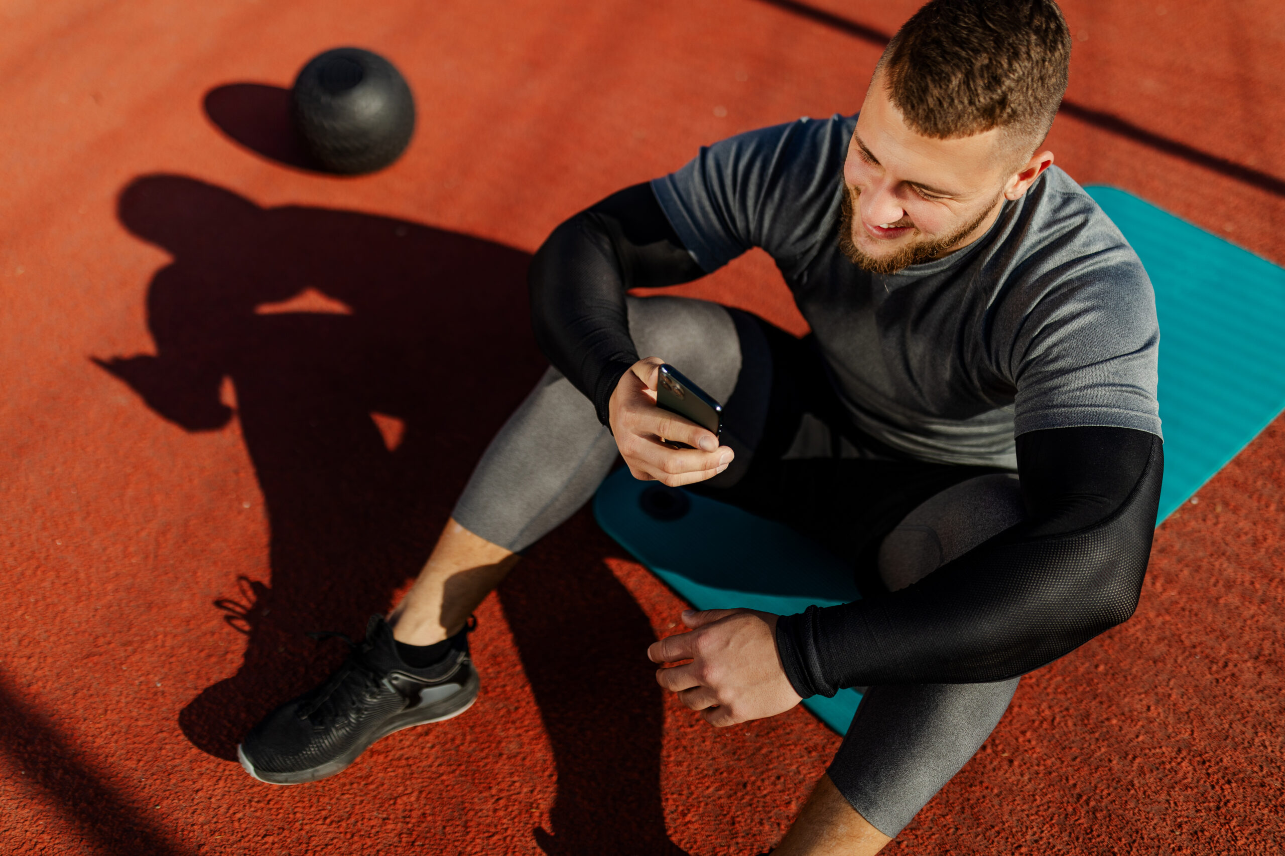 Important Meta Update, image of a muscular man sitting on a blue yoga mat, looking at his phone in his right hand.