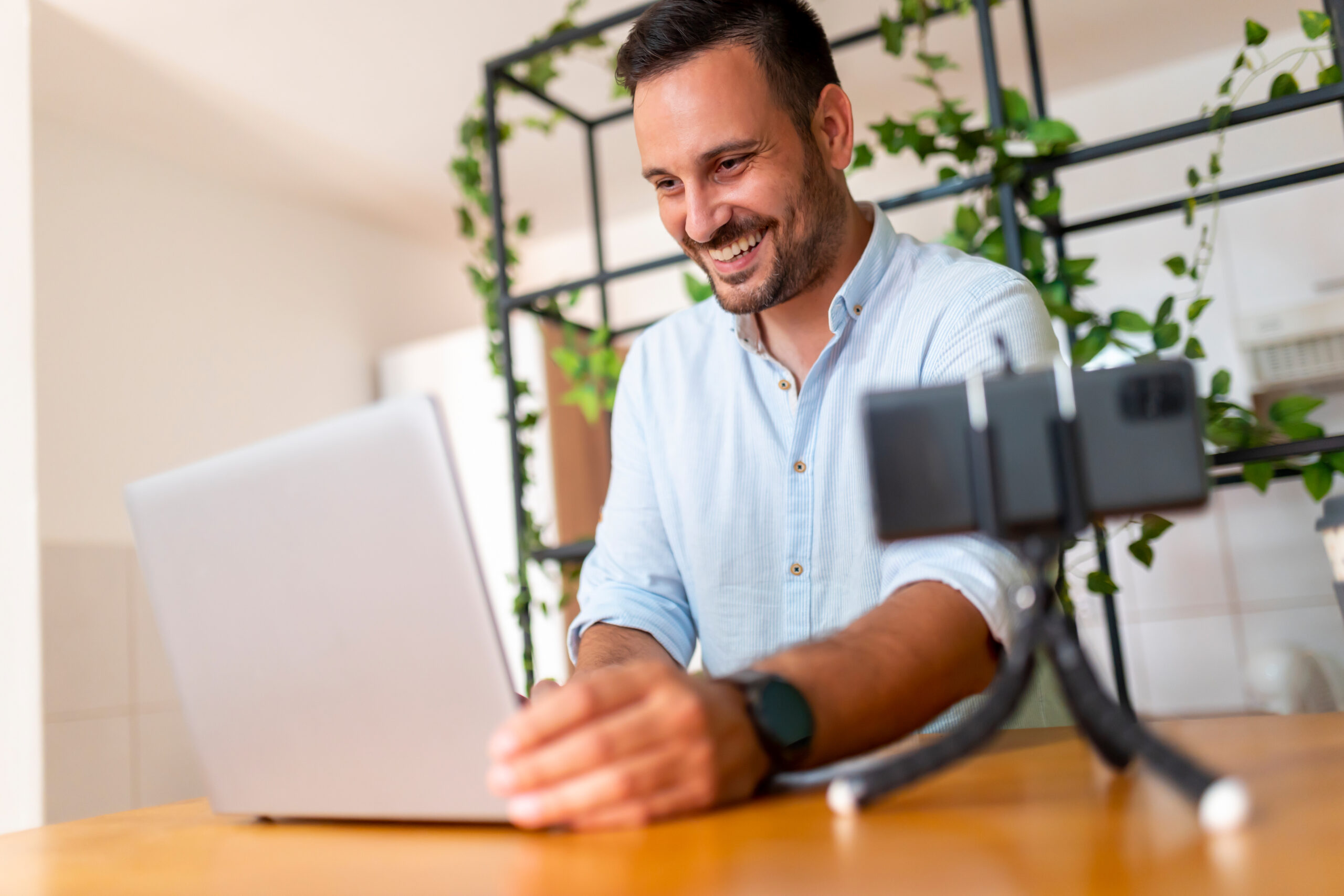 SEO for YouTube, image of a man using his laptop at his desk, with his smartphone propped on a stand, on the table, to his left.