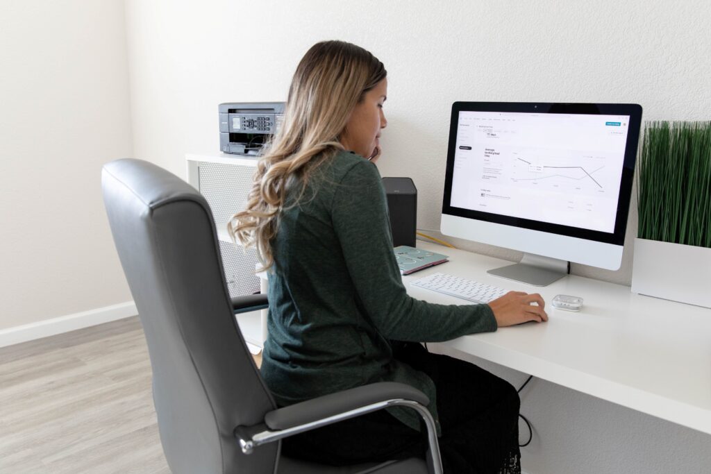 The Best EHR Systems for Small Practices, image of a woman sitting in a gray cushion office chair at her desk using her desktop computer.