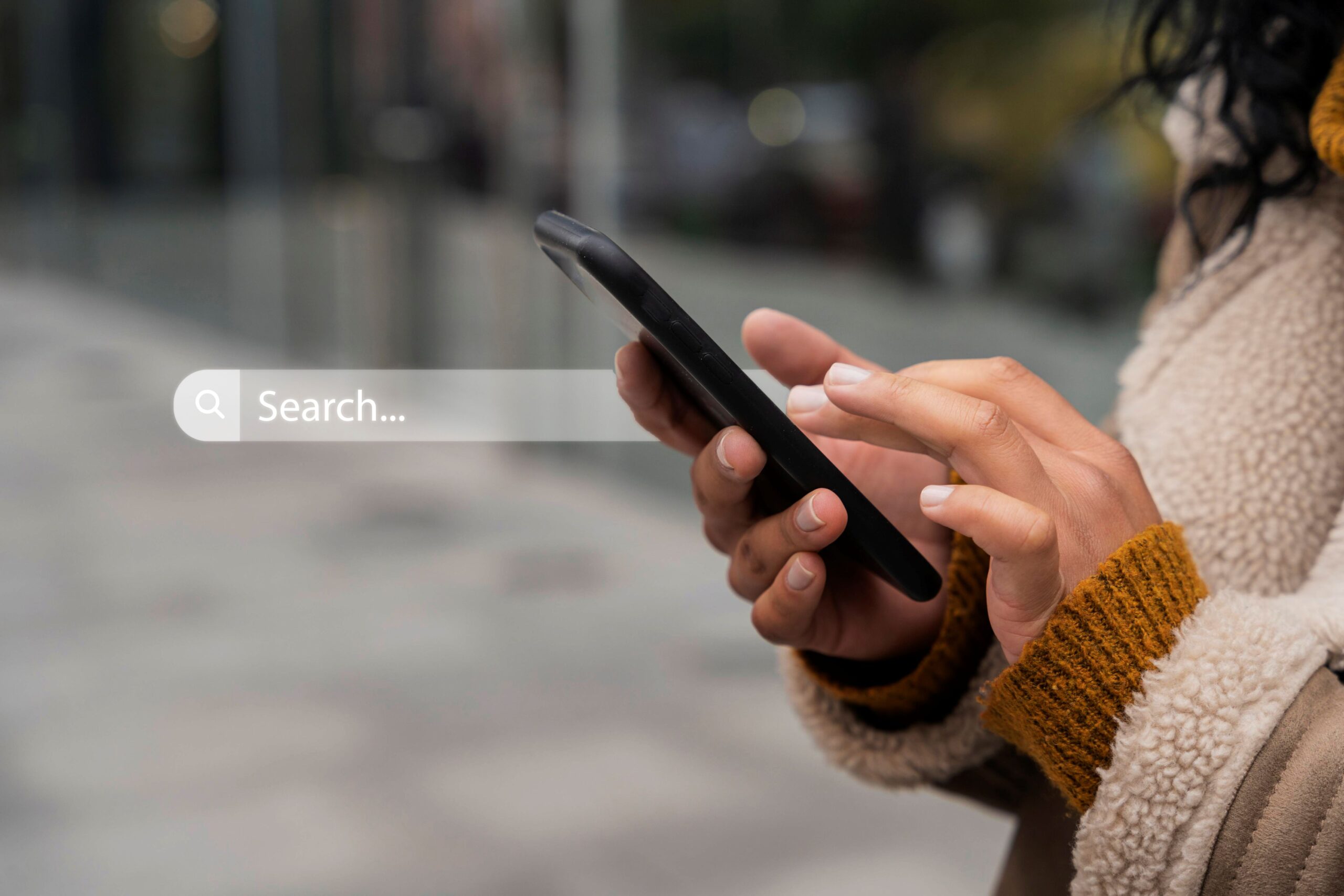 What Does It Mean to Be Everywhere Potential Patients Are Searching, image of a woman wearing a dark yellow sweater and fluffy tan coat uses her smartphone to search.