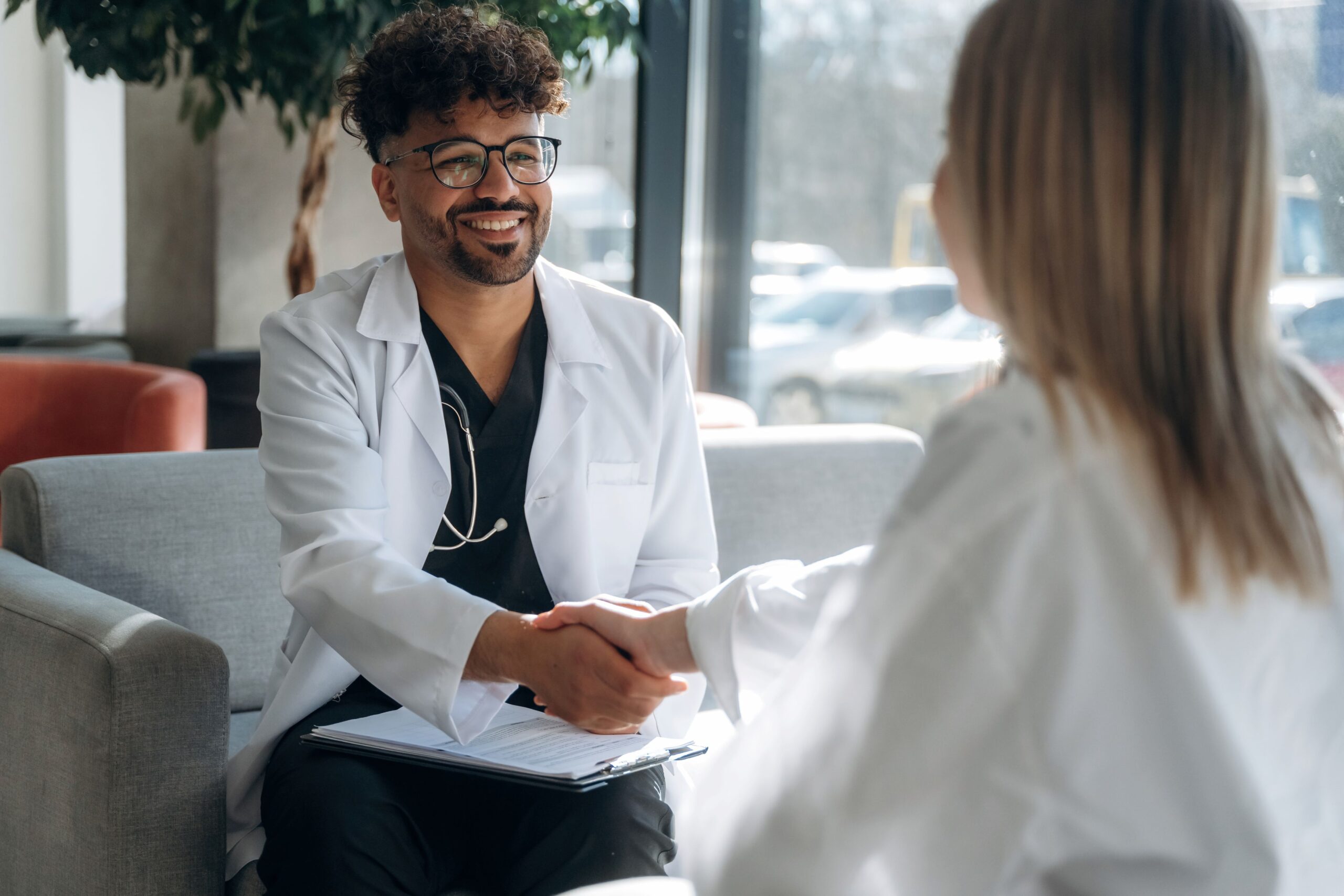 What Does It Mean to Be Everywhere Potential Patients Are Searching, image of a male doctor sitting on a gray couch shaking hands with a female patient wearing a white blouse.