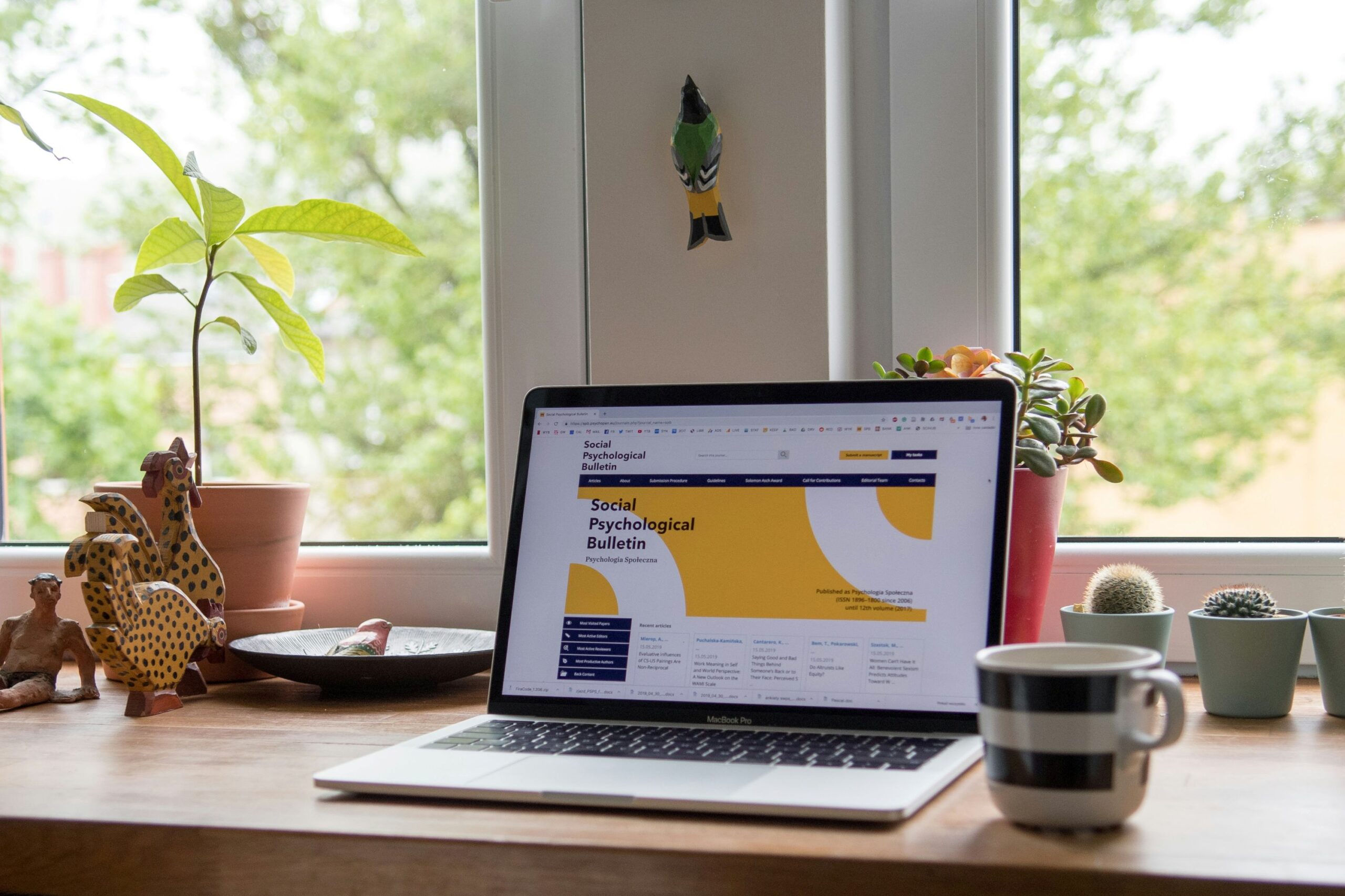 Wix vs WordPress, image of a desk with plants, animal figurines, a coffee cup and an open laptop with “Social Psychological Bulletin” webpage on the screen.