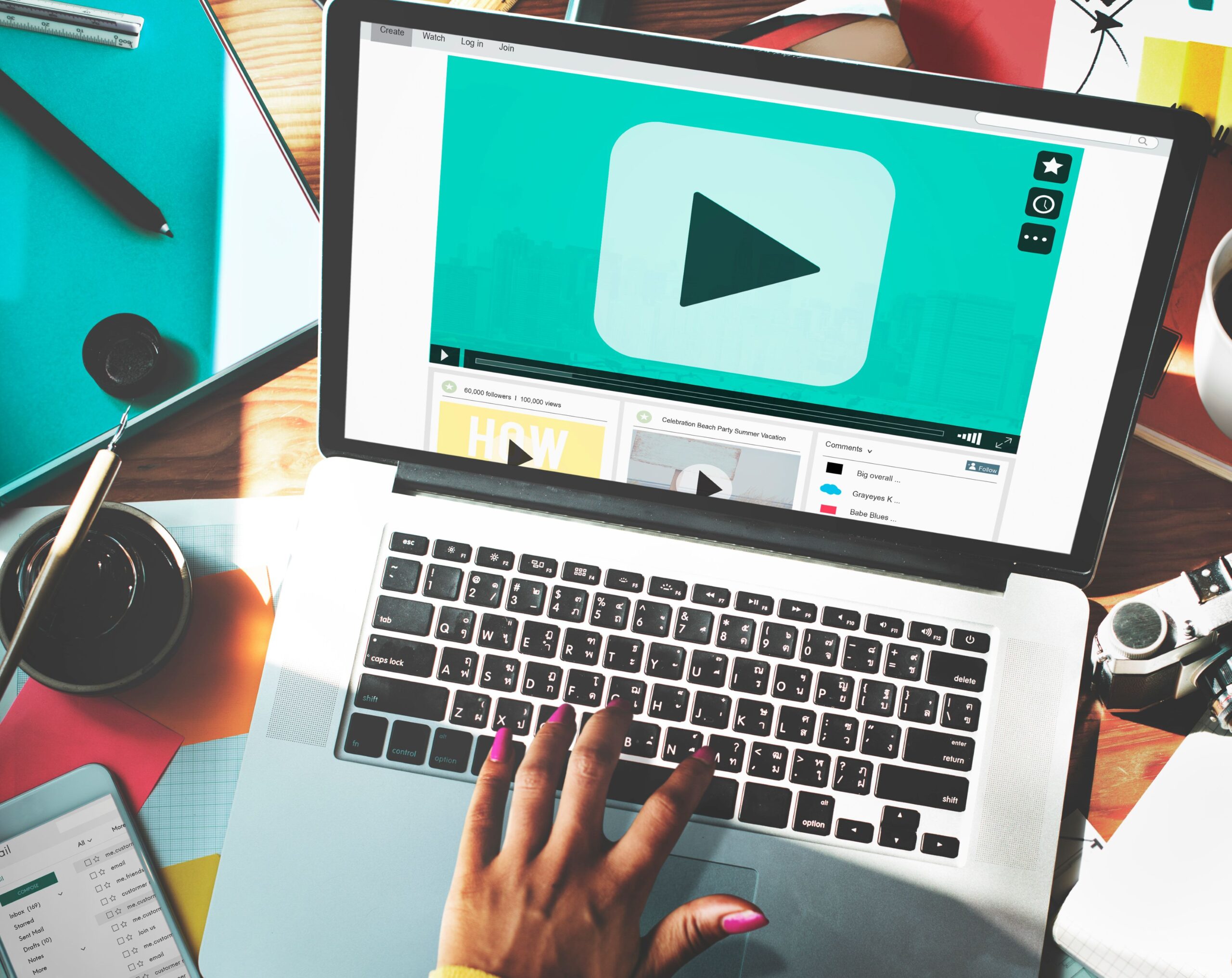 Youtube policies, image of a woman’s hand with pink nail polish typing on a laptop surrounded by many office supplies with a video on screen.