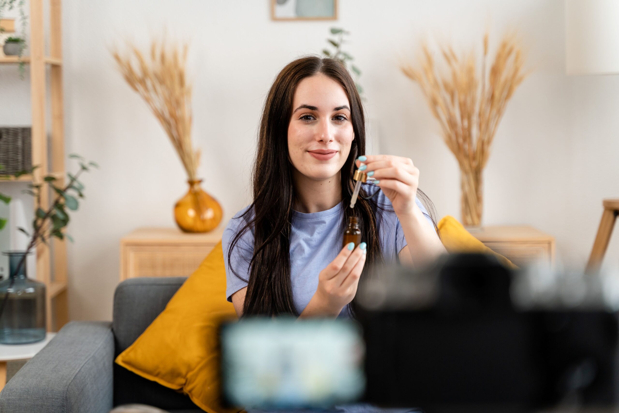 Youtube policies, image of a woman in a light blue t-shirt demonstrating a beauty product on a gray couch in front of a camera.