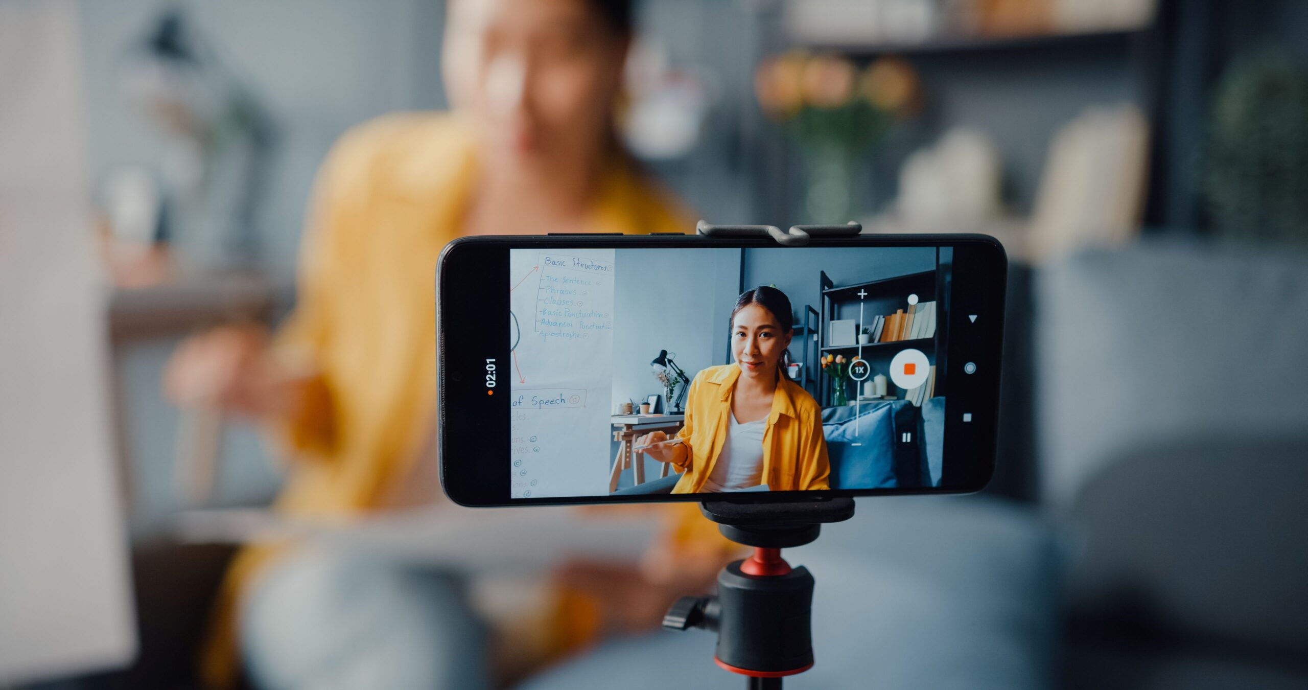 Youtube policies, image of a woman in a yellow button-down shirt recording herself using an iphone on a camera stand.