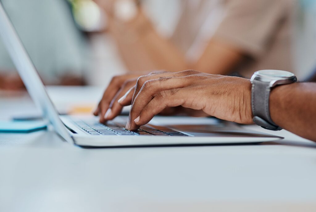 Best WordPress plugins, image of hands typing on a laptop with a watch with gray leather strap on the person’s left wrist.