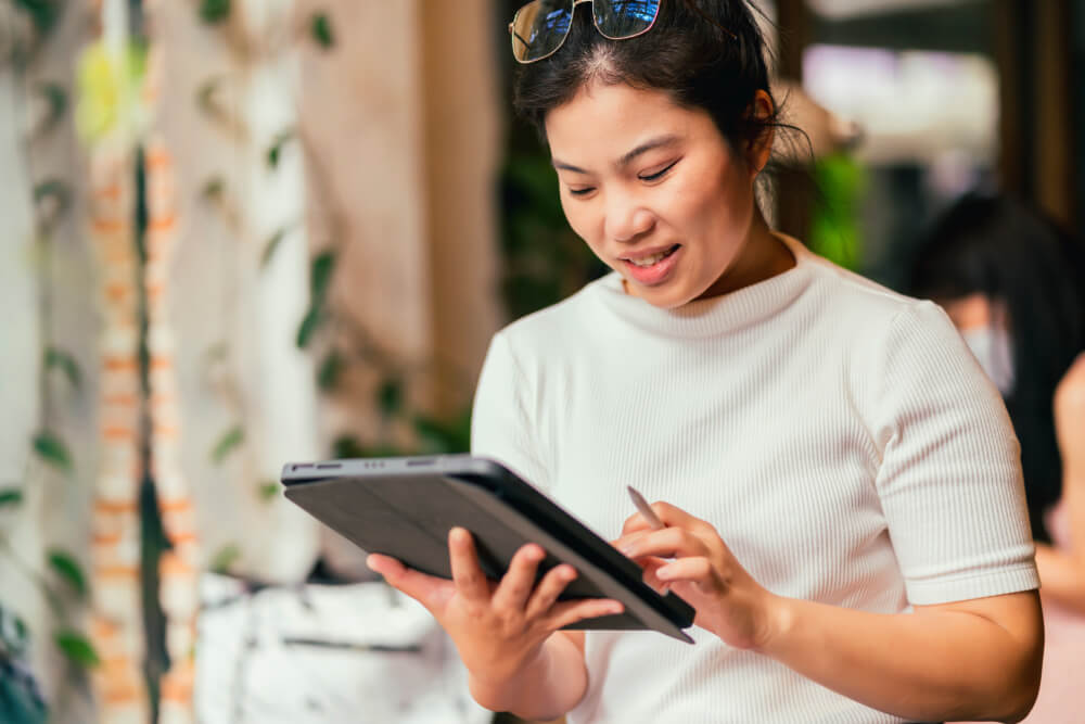 Ebook in libraries, image of a woman wearing a white sweater short sleeve shirt holding a digital table in her right hand and a stylus pencil in her left hand.