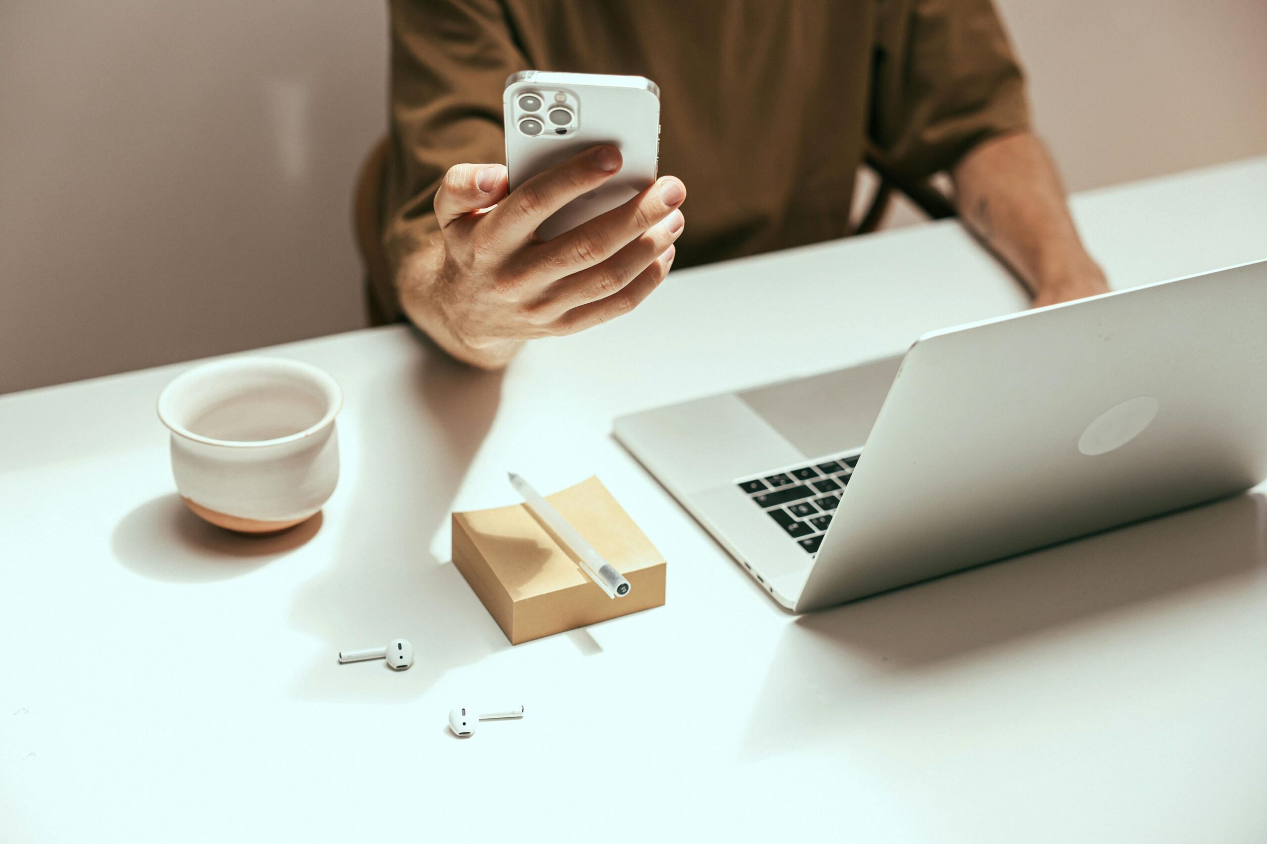 Gmail’s promotions tab, image of a man at his desk holding a phone in his right hand with his opened laptop, post-it notes, pen, airpods, and ceramic cup in front of him.