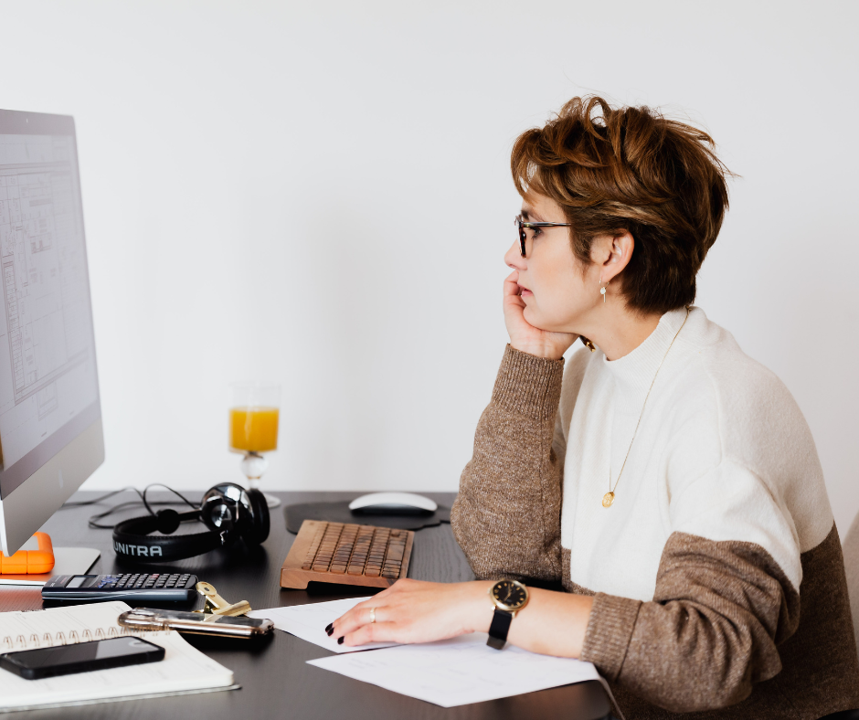 The Future of Local Search in Healthcare, SEO for AI, image of a woman in a cream and brown sweater with short cropped hair and dark framed glasses, looking at her computer screen with a serious expression and her chin in her hands.