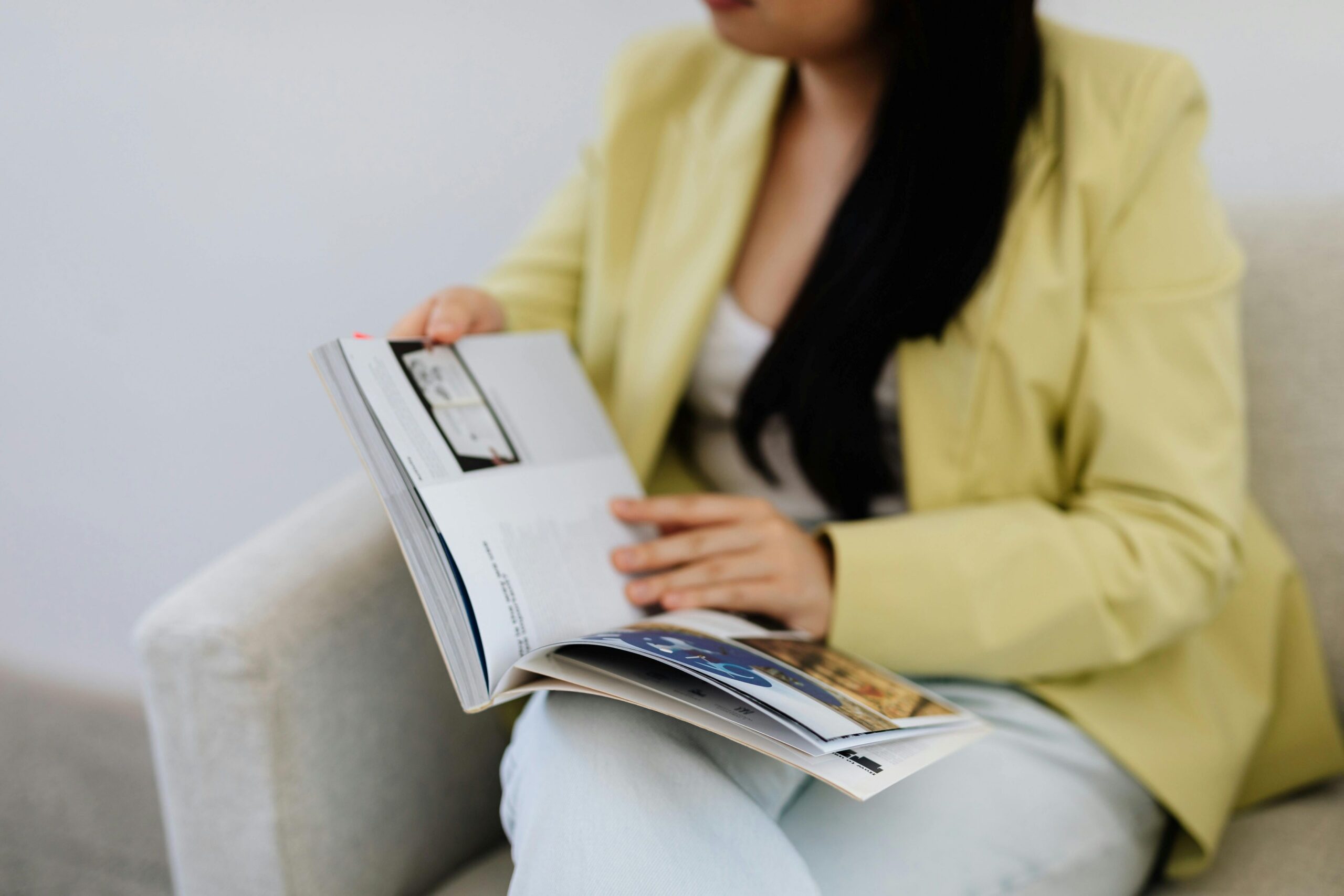 Optimizing your book on Amazon KDP, woman in a yellow jacket sits on a white sofa holding an open book in her lap.