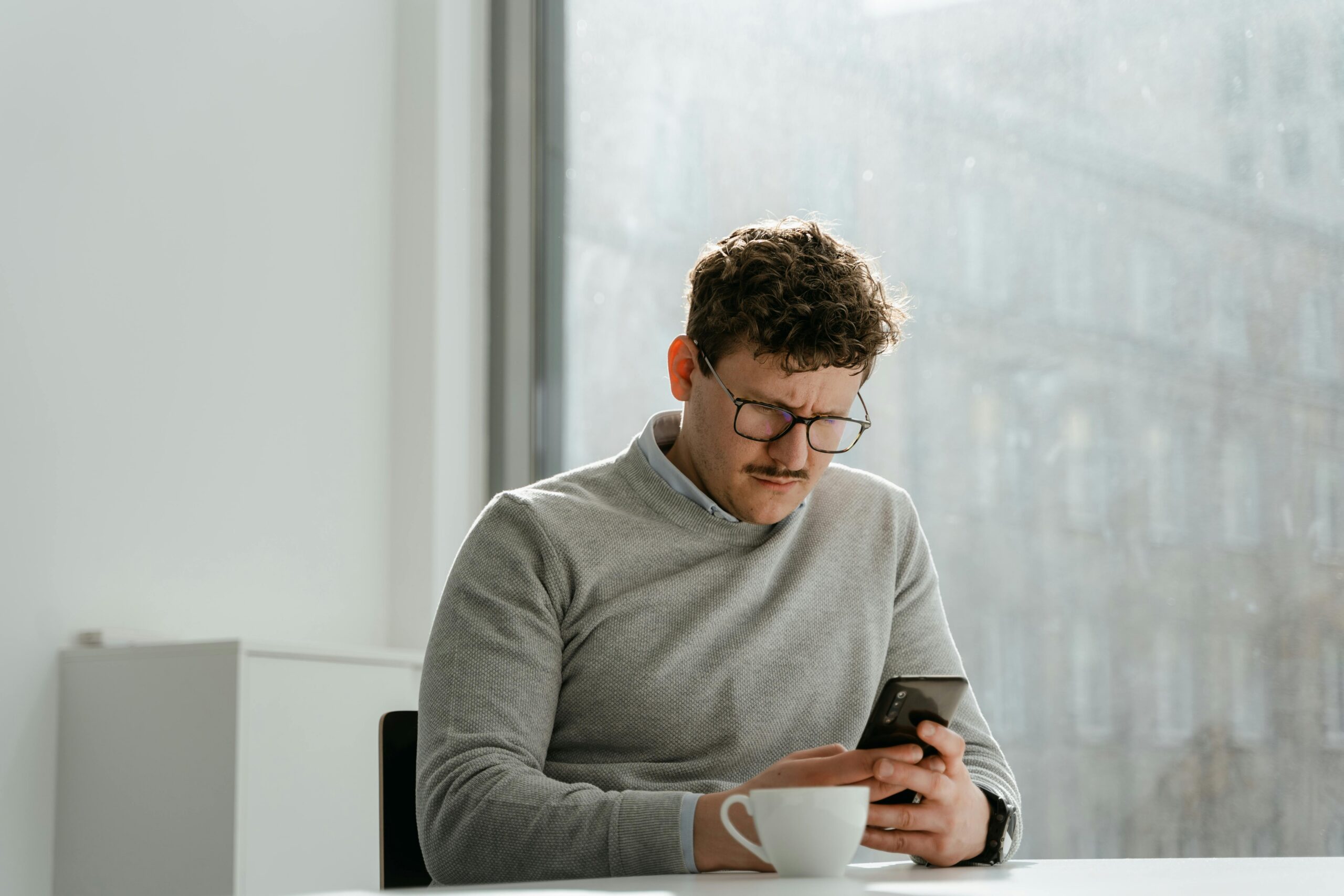 online reputation management, online therapy reviews, image of a man sitting at a table looking down at his phone with a worried expression.