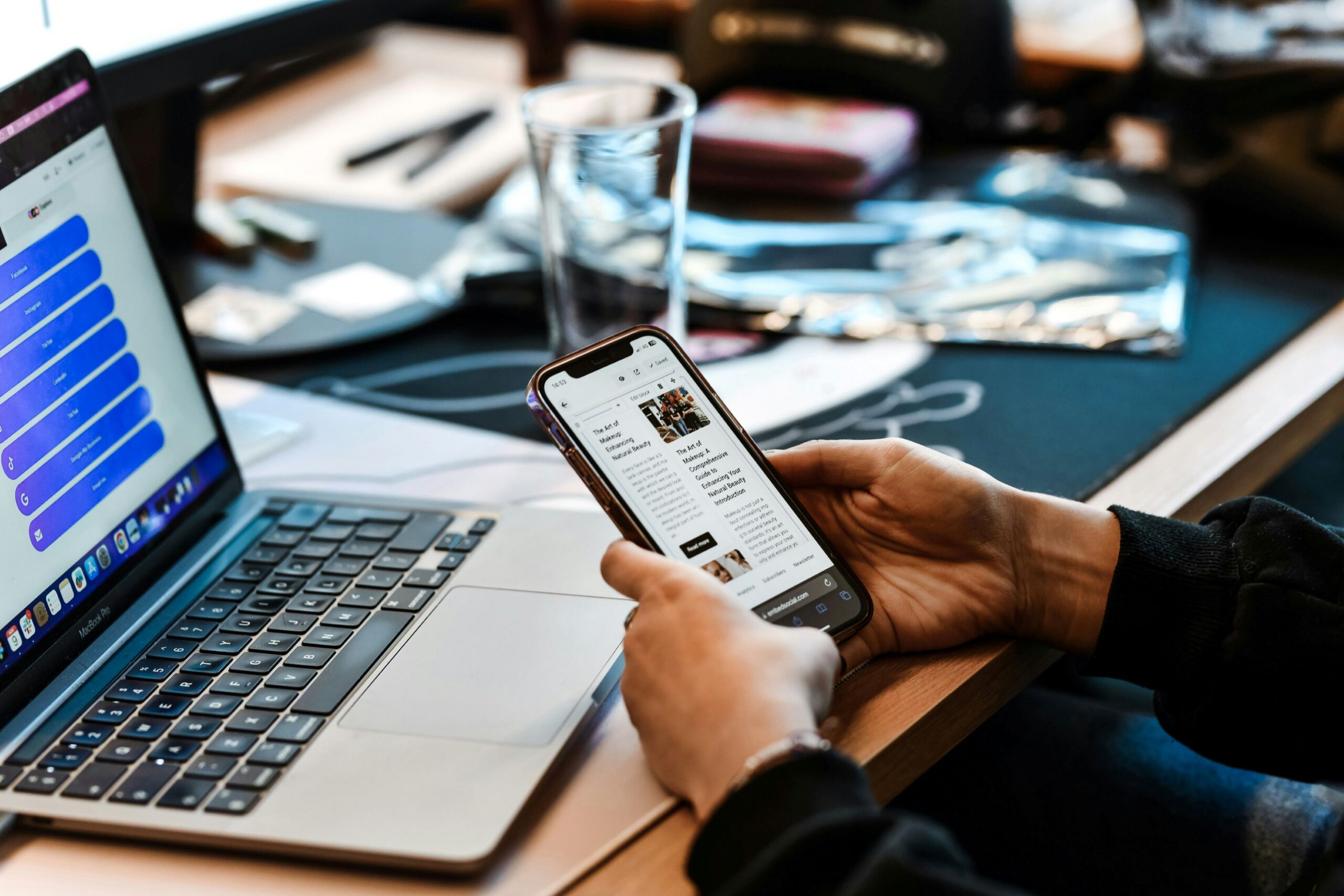 A person holds a smartphone while a laptop showing a social media link management dashboard sits open in the background on a desk. Linktree Alternatives.