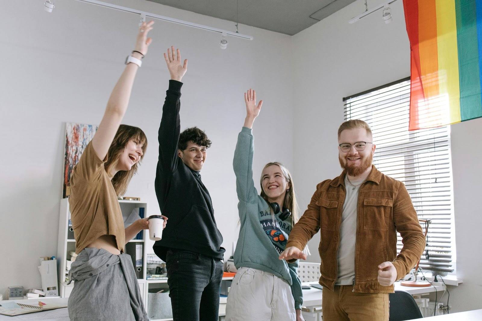 LGBT therapy directories, image of a happy group of youths with an adult man in an office with a pride flag.