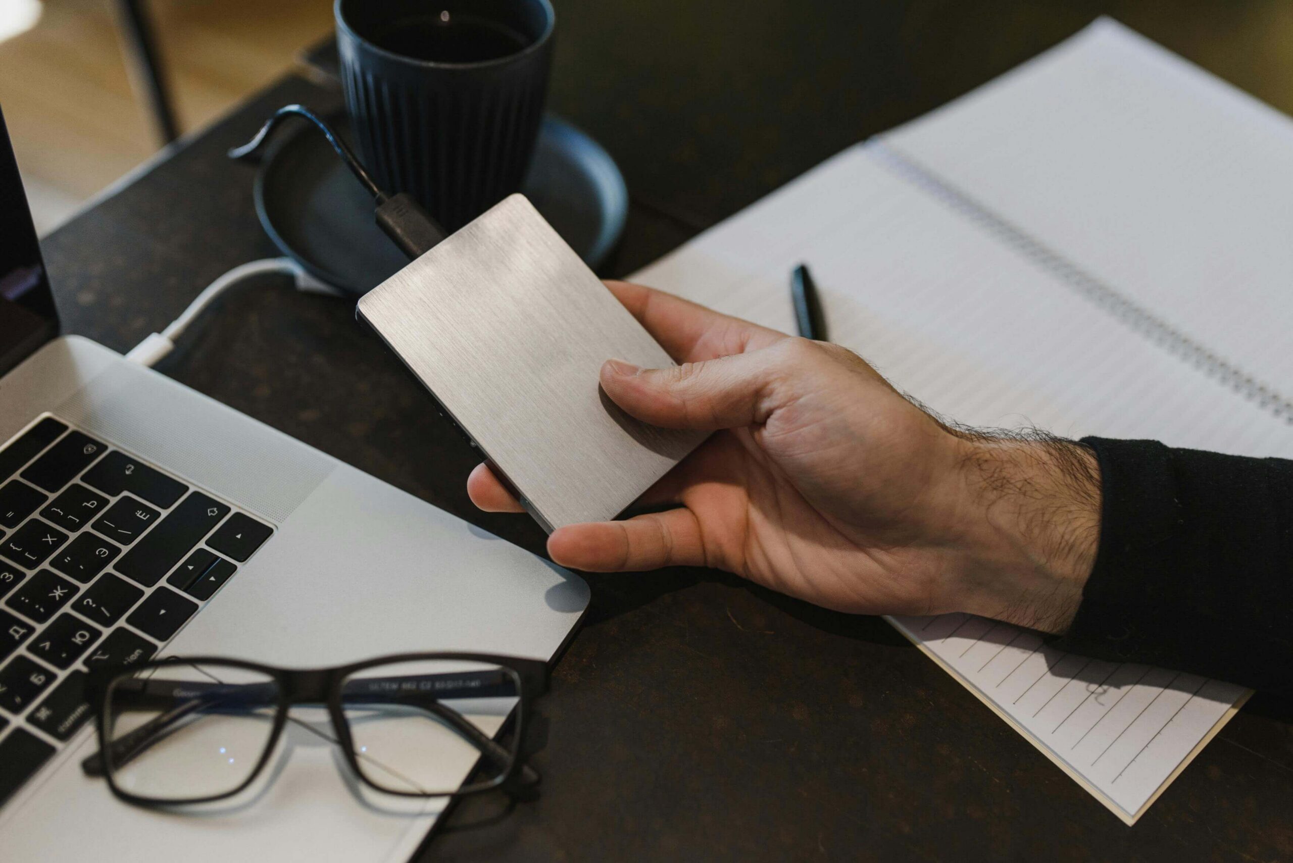 Image of a man’s hand holding a local hardware device next to his laptop and glasses.