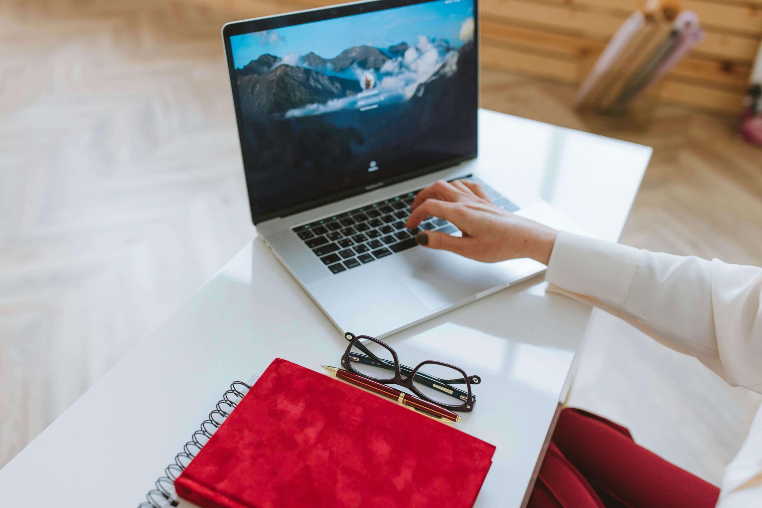 Image of a woman’s hand typing her password into a laptop on a white desk.