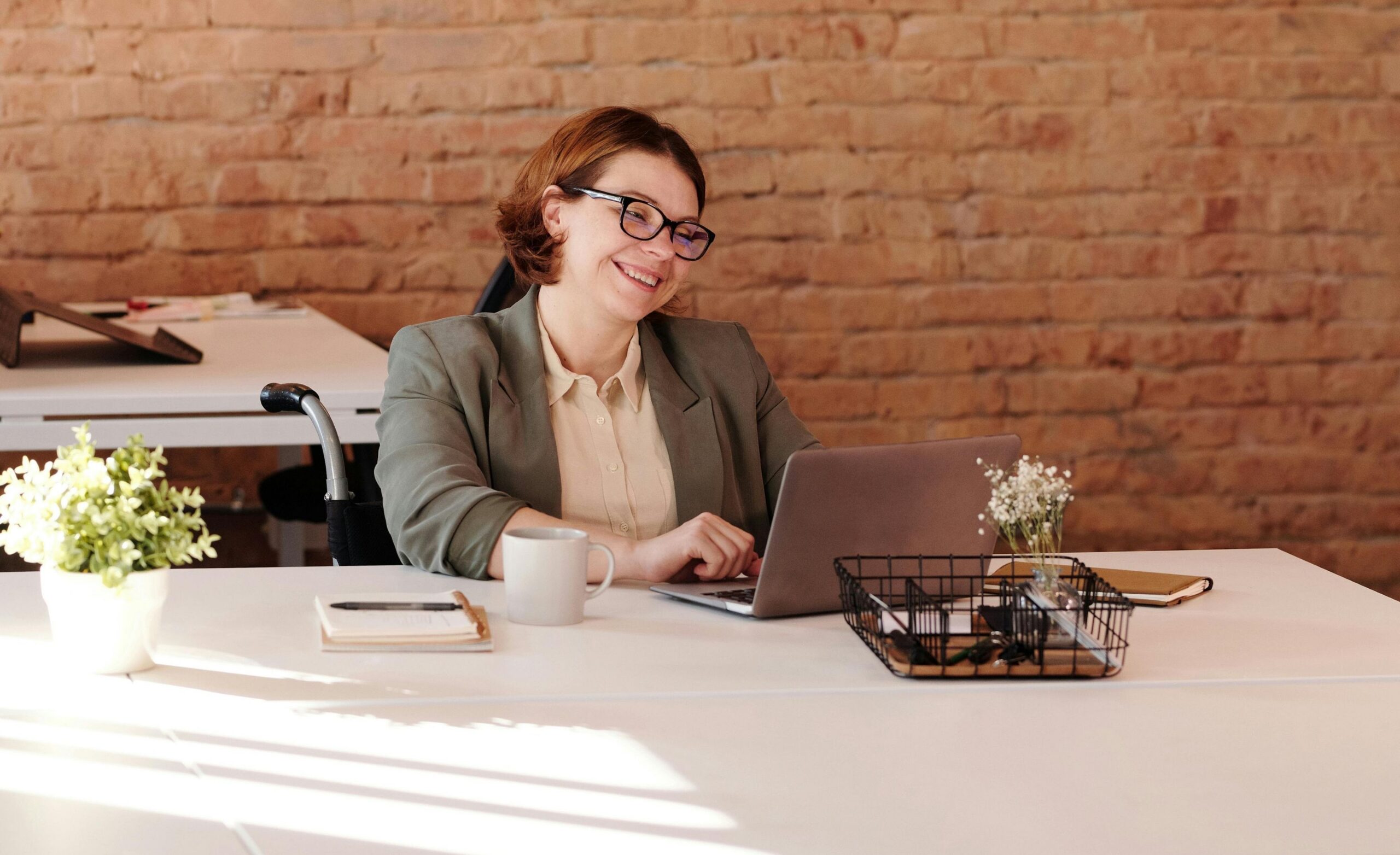 Image of a professional woman sitting in a wheelchair working on her laptop at a white desk.