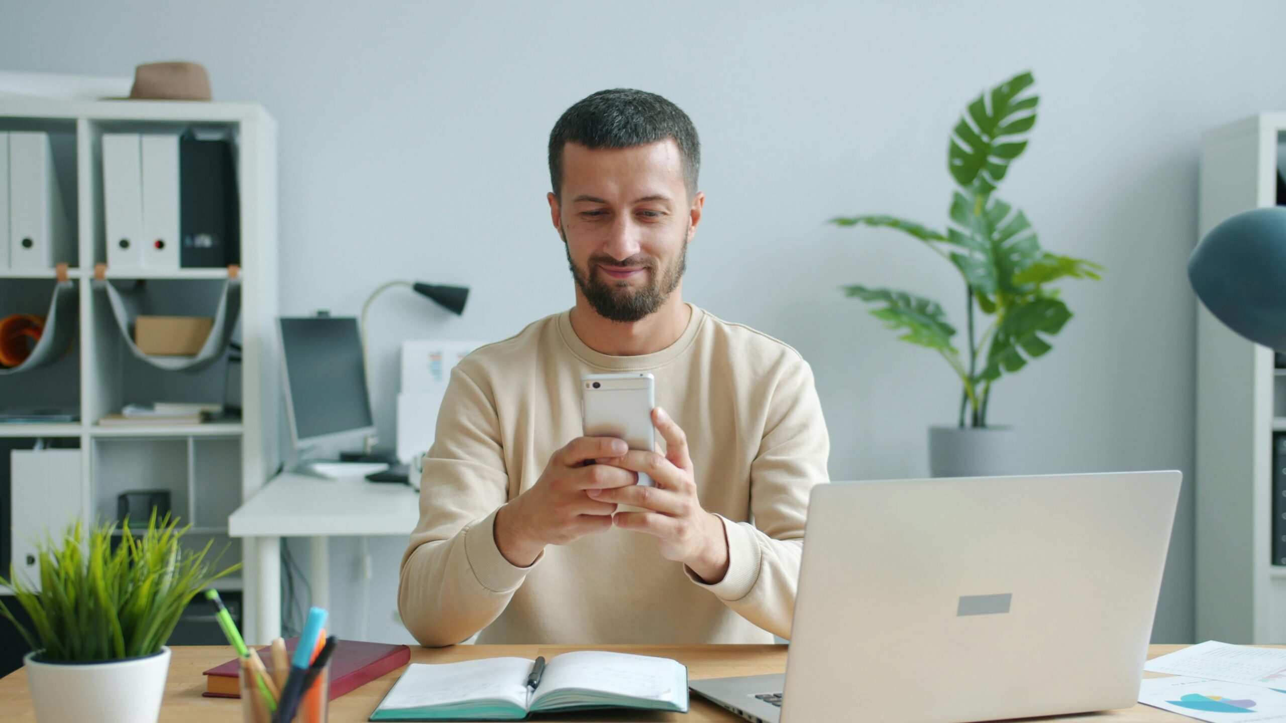Image of a man at a desk smiling at the cell phone in his hands.