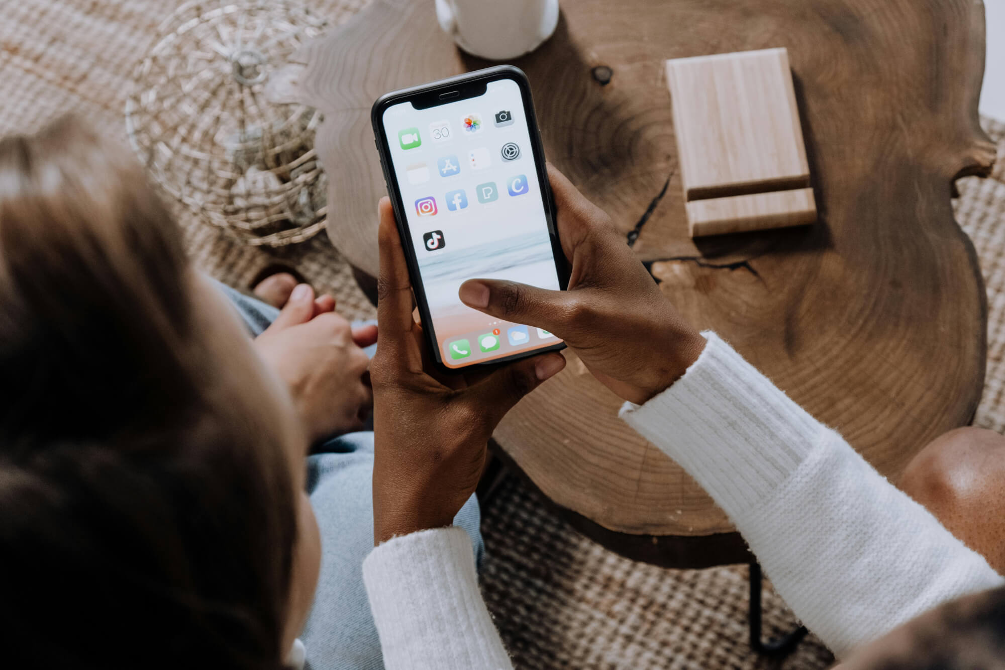 Image of a woman’s hands showing her cell phone with social media icons on the screen to another woman.
