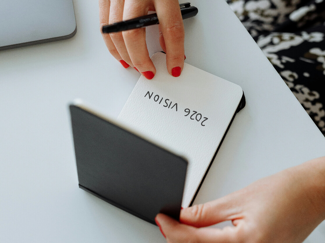 Image of hands writing “2026 vision” in a small notebook at a desk.
