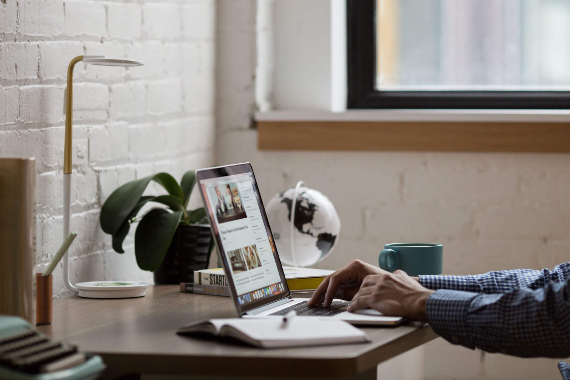 Image of hands typing on a laptop keyboard with blog images on the screen.