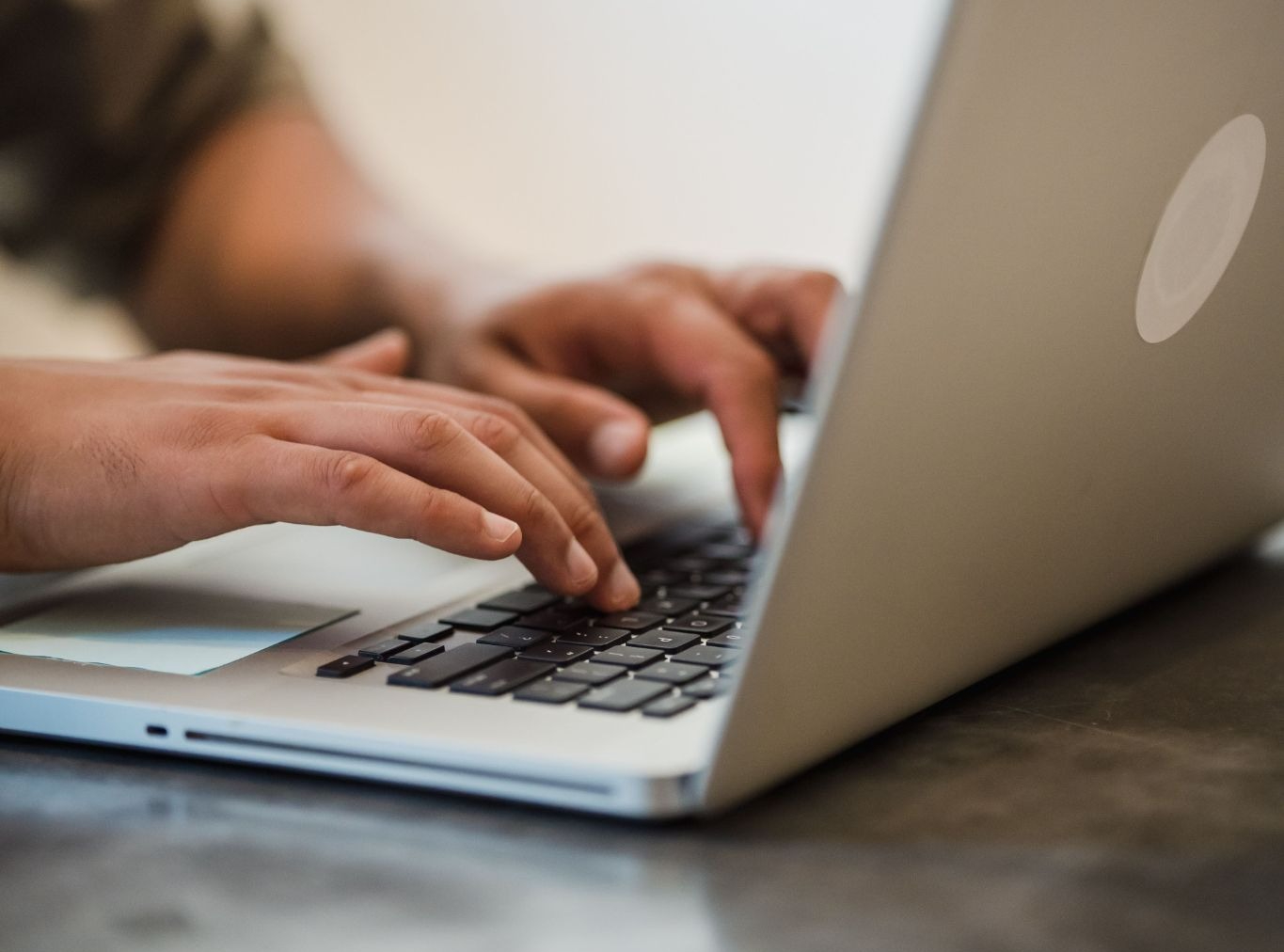 image of a close up of two hands typing on a laptop on a dark grey desk.