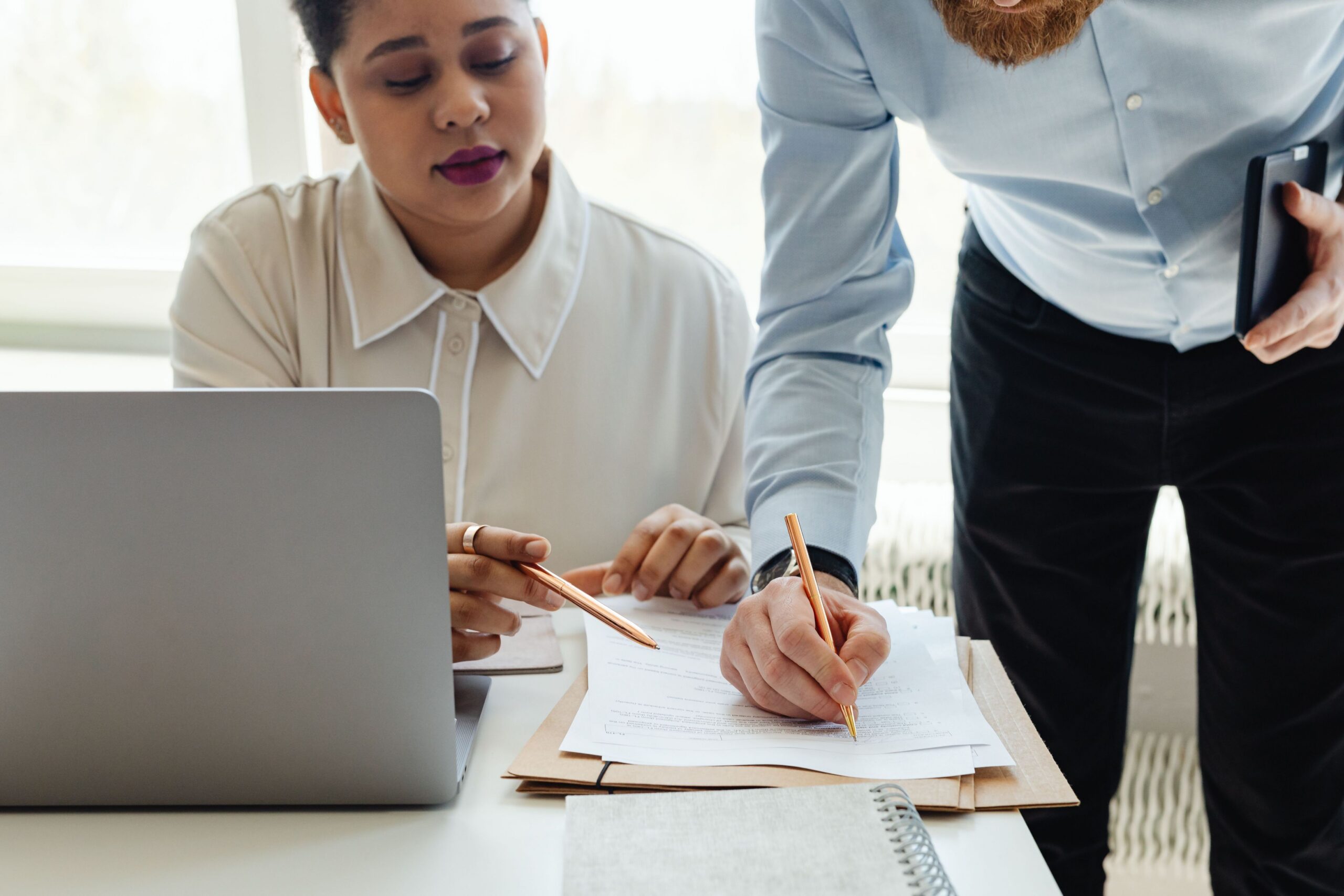 A woman sits at her desk and goes over paperwork with a man to create a plan to ensure patient safety and data security.