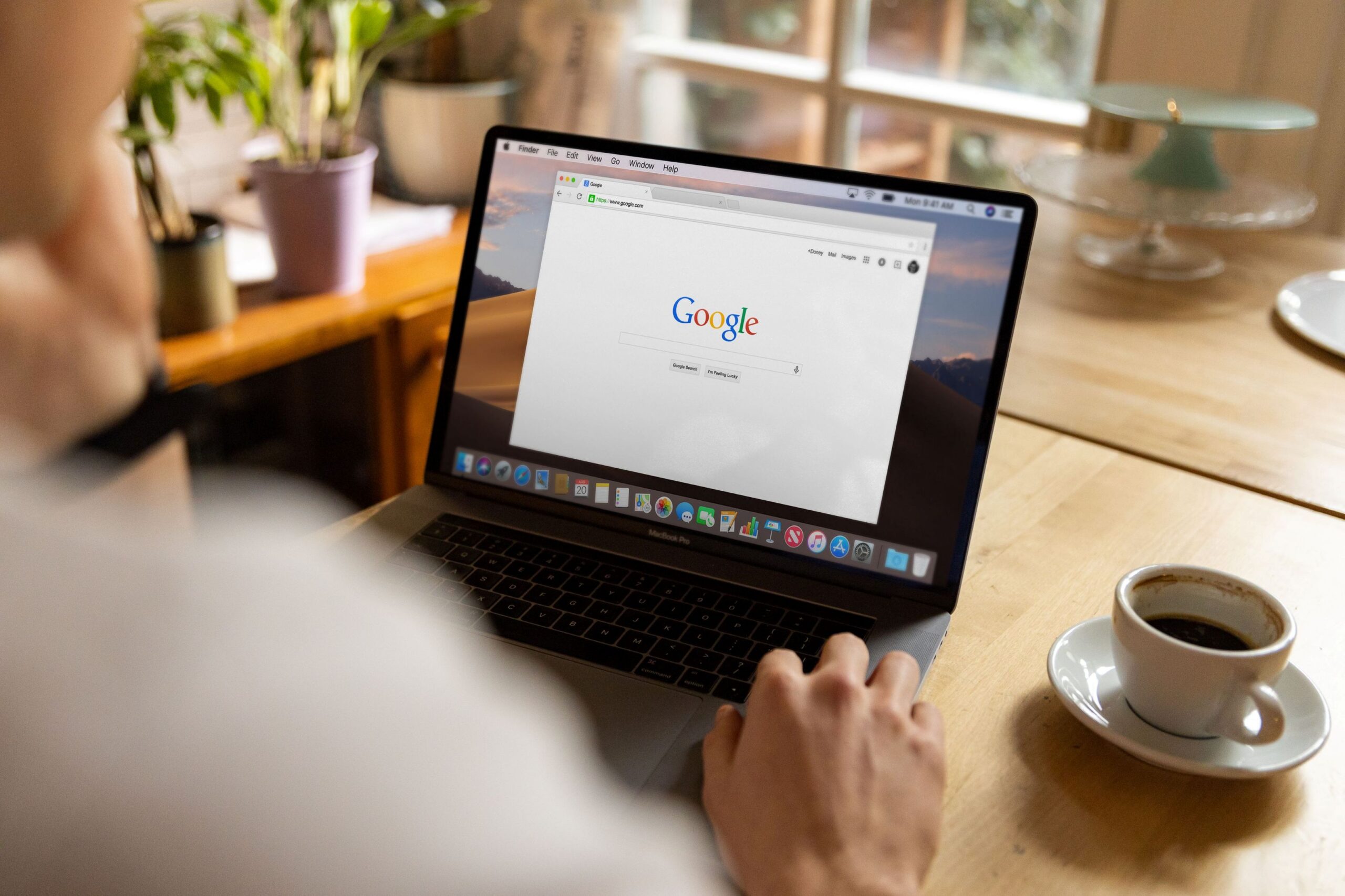 A man sits at a wood table with a cup of coffee and uses an internet search engine that uses Natural Language Processing