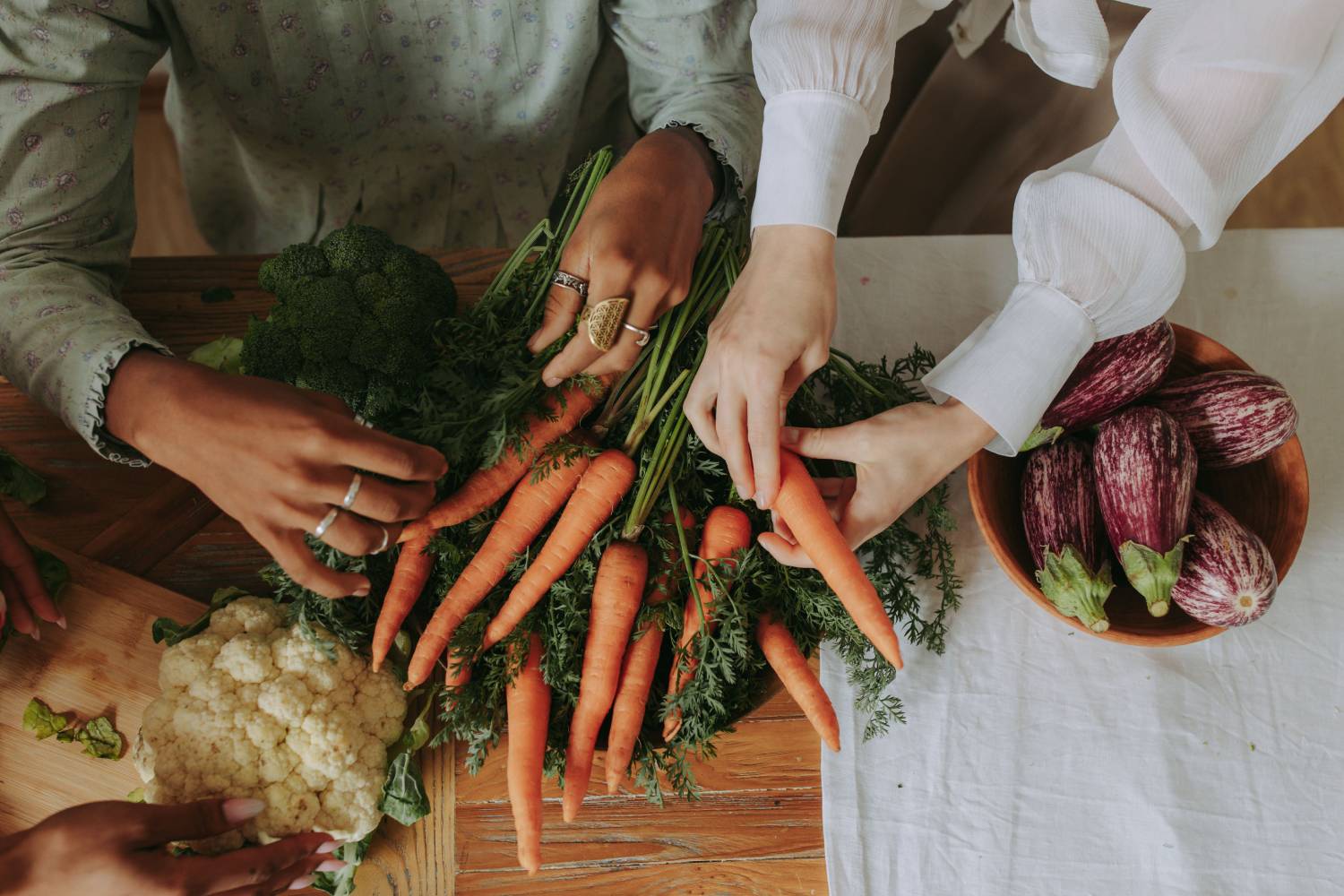 A nutritionist sits at a table full of vegetables teaching clients while holding a carrot.