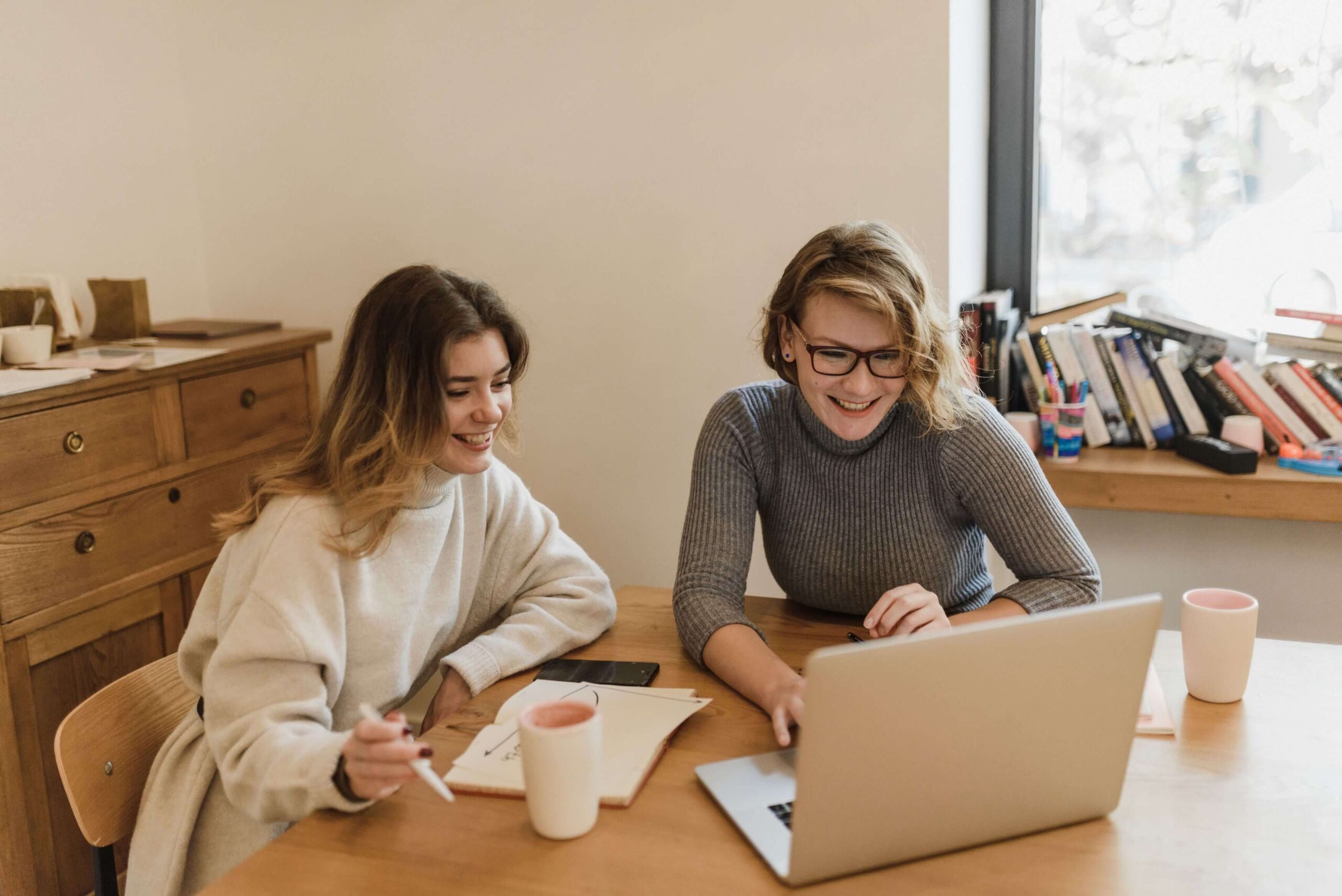 image of two women sitting at a table and working together on a laptop