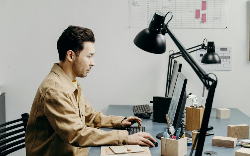 fake cloudflare malware, image of a professional man sitting at a grey table filled with two computer monitors and office supplies.